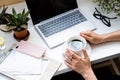 Woman`s hands holding cup of coffee in cozy office with laptop and green plants Royalty Free Stock Photo