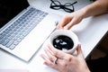 Woman`s hands holding cup of coffee in cozy office with laptop and green plants Royalty Free Stock Photo