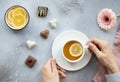 Woman`s hands holding a cup of hot tea with lemon and various sweets on a gray background with flowers. Royalty Free Stock Photo