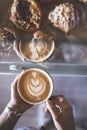 Woman`s hands holding a cup of signature coffee prepared by a barista next to a counter full of croissants. Restaurant. Quiet Royalty Free Stock Photo