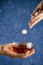 Woman`s hands holding cup with warm splashing black tea and dropping sugar cubes Royalty Free Stock Photo