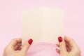 Woman`s hands are holding empty mock-up brochure for writing letter above pink background