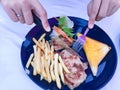 The woman`s hands are holding a fork and knife to cut the steak.  This is Grilled Pork chop Steak with gravy sauce, there are Royalty Free Stock Photo