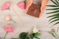 Woman`s hands holding a gift box on gray wooden background with beautiful flowers and green leaves. Royalty Free Stock Photo