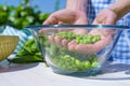 Woman`s hands holding a handful of freshly picked peas inside a glass bowl outdoors in the rays of the sun
