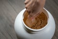 Woman`s hands holding measuring scoop of whey protein powder over jar