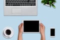 Woman`s hands holding modern tablet over blue background. Office desk with laptop computer, flower, cell phone, tablet and cup of Royalty Free Stock Photo