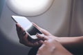 Woman`s hands holding and pointing at a white smart phone with blank black desktop screen next to an airplane window Royalty Free Stock Photo