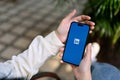 A woman\'s hands holding a smartphone with LinkedIn logo on screen, iPhone with LinkedIn logo