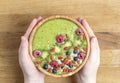 Woman`s hands holding smoothie bowl. Breakfast kiwi smoothie bowl with with raspberries, blueberries, Goji berries and coconut.