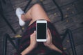 Woman`s hands holding white mobile phone with blank black screen on thigh with wooden floor background in vintage cafe Royalty Free Stock Photo