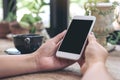 Woman`s hands holding white mobile phone with blank blank desktop screen and coffee cup on table in cafe Royalty Free Stock Photo