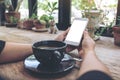 Woman`s hands holding white mobile phone with blank desktop screen and coffee cup on table in cafe Royalty Free Stock Photo