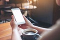 A woman`s hands holding white mobile phone with blank desktop screen with coffee cup on wooden table in cafe Royalty Free Stock Photo