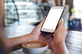 A woman`s hands holding white mobile phone with blank desktop screen with coffee cup on wooden table in cafe Royalty Free Stock Photo