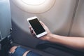 Woman`s hands holding a white smart phone with blank black desktop screen next to an airplane window Royalty Free Stock Photo