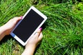 Woman`s hands holding white tablet with blank skreen on green gr