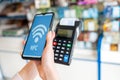 A woman`s hands holds a payment terminal with a check and pays for a purchase using a smartphone.On the phone screen-wi-fi networ