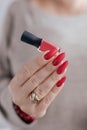 Woman`s hands with long nails and a bottle of red orange nail polish Royalty Free Stock Photo