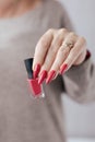 Woman`s hands with long nails and a bottle of red orange nail polish Royalty Free Stock Photo