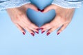 Woman`s hands making heart symbol. Female hands in blue knitted sweater fabric with beautiful glossy manicure