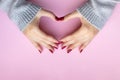 Woman`s hands making heart symbol. Female hands in a gray knitted sweater fabric with beautiful glossy manicure