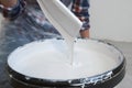 WomanÃ¢â¬â¢s hands mixing a gallon of grey paint with wooden paint stirring stick.