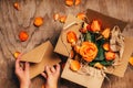 Woman`s hands open craft paper envelope next to open box with orange roses in it, close up.