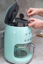 Woman`s hands are pouring ground coffee into a SMEG brand coffee maker on the kitchen table