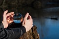 Woman`s hands protecting Clear Quartz Sphere on bark, rhytidome, reflecting lake, forest and sky