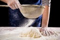Woman`s hands sifts flour through a sieve on the dough