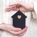 Woman`s hands surround a model of a dark house. Real estate and insurance concept. Protecting the family from the coronovirus