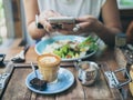 Woman`s hands taking photo of coffee cup on wooden table by smartphone Royalty Free Stock Photo