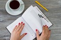 Woman`s hands turning a page in a notebook. Cup of tea and a pen Royalty Free Stock Photo