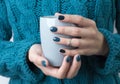 Woman`s hands with turquoise manicure hold a grey cup of coffe or tea