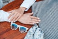 Woman`s hands on a wooden table with a knitted bag and sunglasses. Top view. Copy, empty space for text