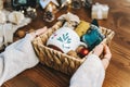 Woman s hands wrapping Christmas eco gift wicker basket, close up. Unprepared presents on wooden table with natural