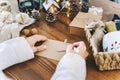 Woman s hands wrapping Christmas gift envelope, close up. Unprepared presents on white table with decor elements and Royalty Free Stock Photo