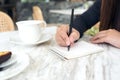 A woman`s hands writing down on a white blank notebook with coffee cup and dessert on table in cafe Royalty Free Stock Photo