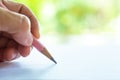 Woman left Hand holding multicoloured pencil Pink & Grey colour, writing letter on white paper, Bokeh green garden background