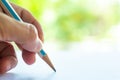 Woman left Hand holding multicoloured pencil White & Blue colour, writing letter on white paper, Bokeh green garden bg. Royalty Free Stock Photo