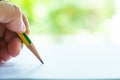 Woman left Hand holding multicoloured pencil Yellow & Green colour, writing letter on white paper, Bokeh green garden Royalty Free Stock Photo