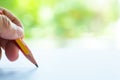 Woman left Hand holding multicoloured pencil Yellow & Red colour, writing letter on white paper, Bokeh green garden bg. Royalty Free Stock Photo