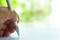 Woman left Hand holding a silver pen, writing letter on white paper, Bokeh green garden background, Notebook, Communication Royalty Free Stock Photo