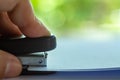 Woman left Hand holding stapler pressing at white paper, Bokeh green garden background, Close up shot, Office, Stationery