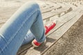 Woman`s legs in a blue jeans and red canvas sneakers sitting on a bench Royalty Free Stock Photo