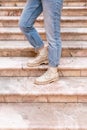 Woman`s legs in blue twisted jeans and in beige boots on pink marble staircase. Front view, vertical photo