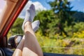 Woman`s legs out of car window. Passenger feels free and happy on road trip. Girl relaxes during ride. Summer traveling Royalty Free Stock Photo