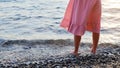 Woman`s legs in pink dress stand barefoot in water on sea pebble shore Royalty Free Stock Photo