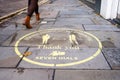 A woman`s legs walk past a yellow Covid 19 social distancing sign painted on the pavement in Covent Garden